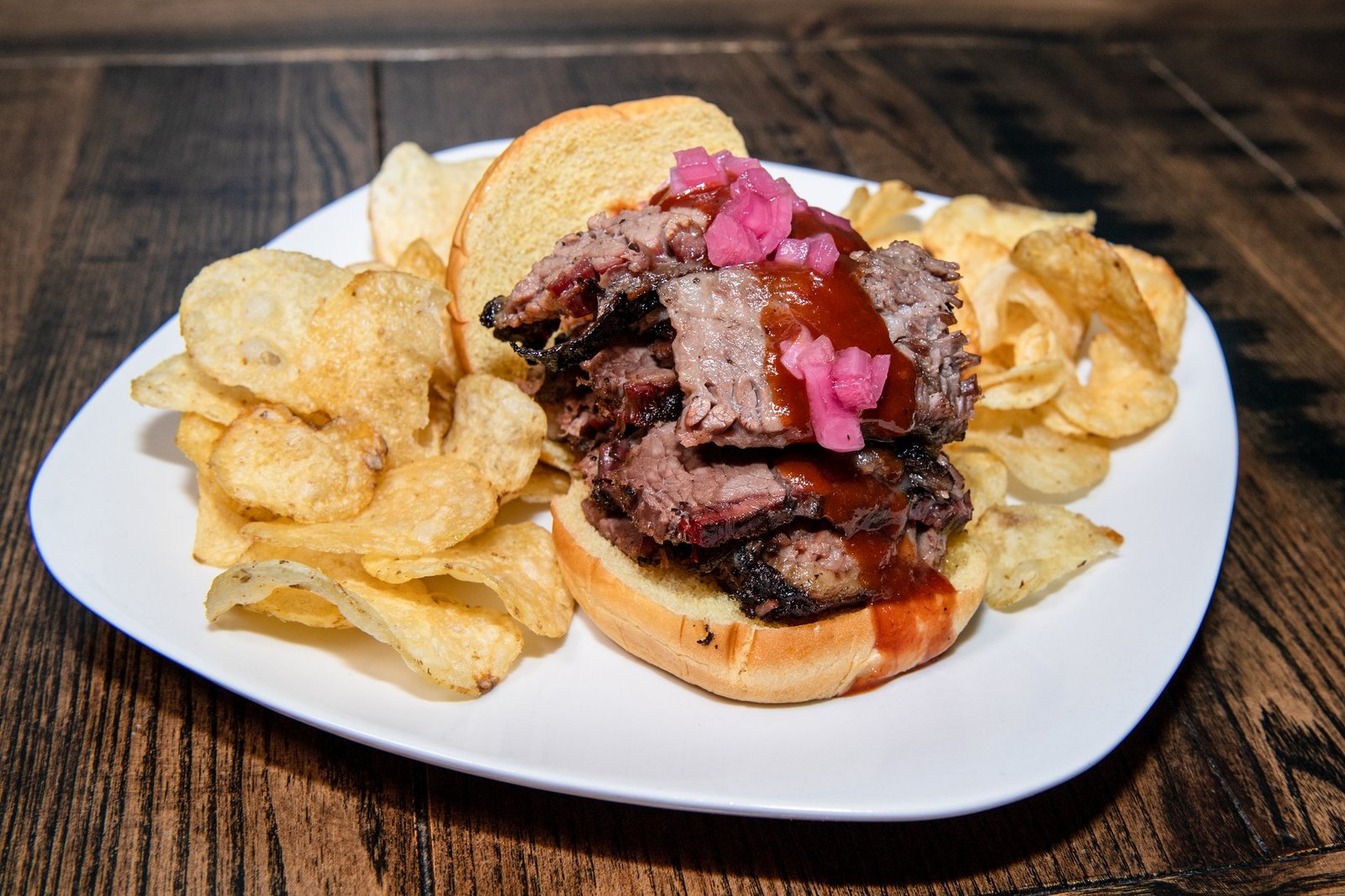 Barbecue beef sandwich with potato chips on a white plate.